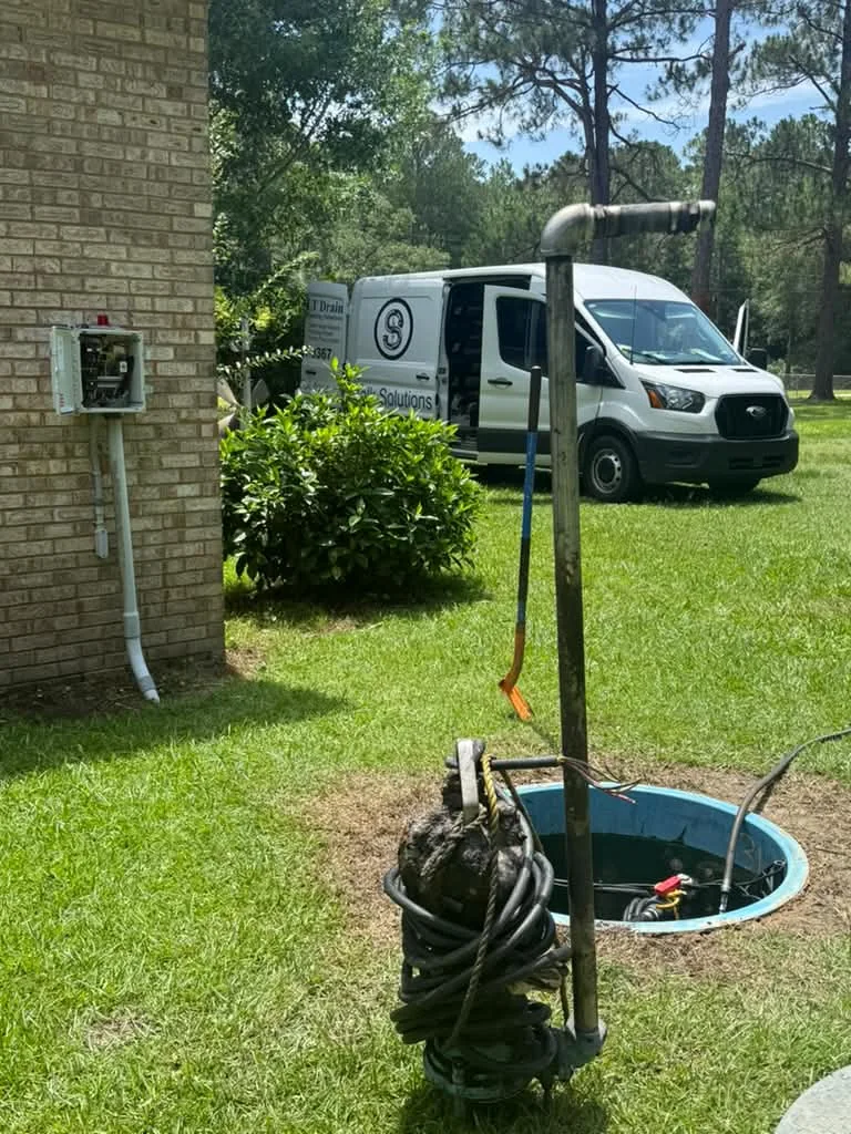 A grinder pump lifted on its guide rail out of the basin in a grass yard, van parked behind