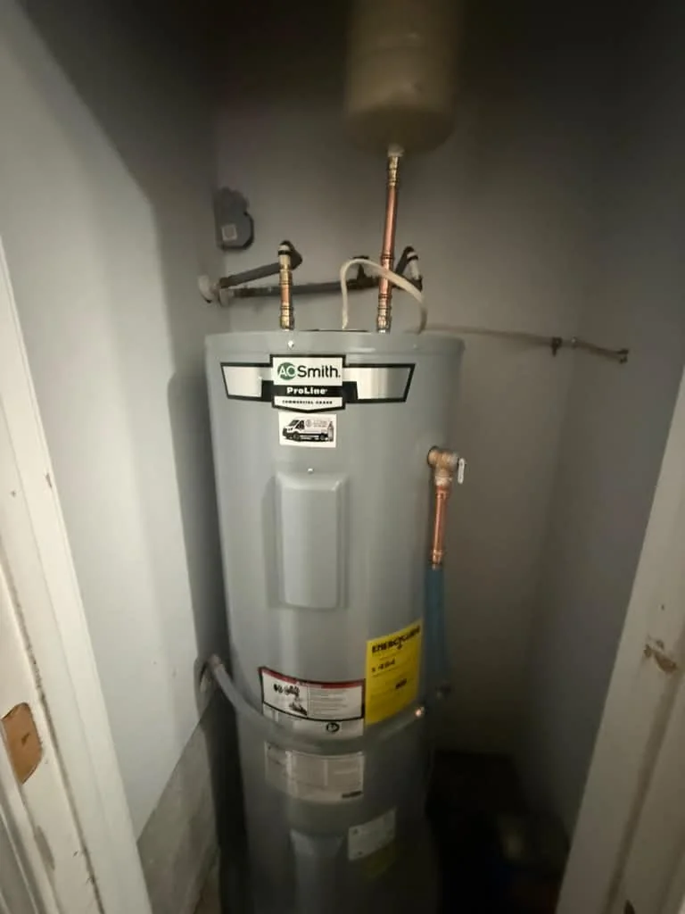 A new A.O. Smith electric water heater in a closet with copper flex connectors and a drain pan