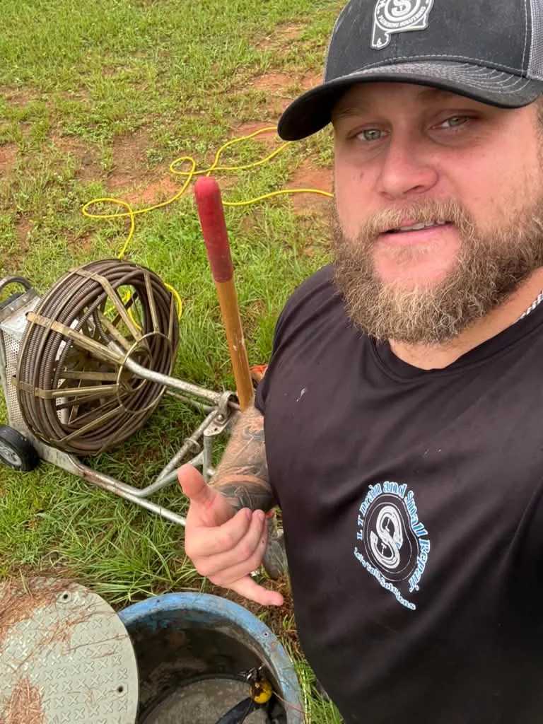 Paul Evans in an LT Drain shirt beside an open sewer cleanout with the drain cable reel at his feet