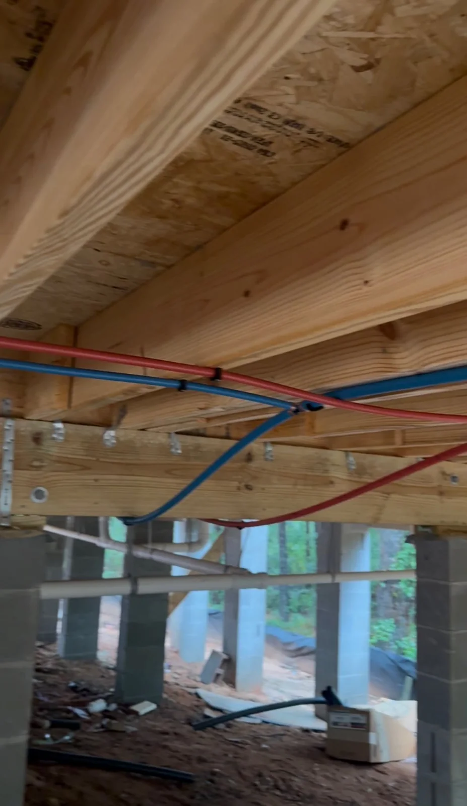 Red and blue PEX lines run along floor joists under a house, replacing older supply piping