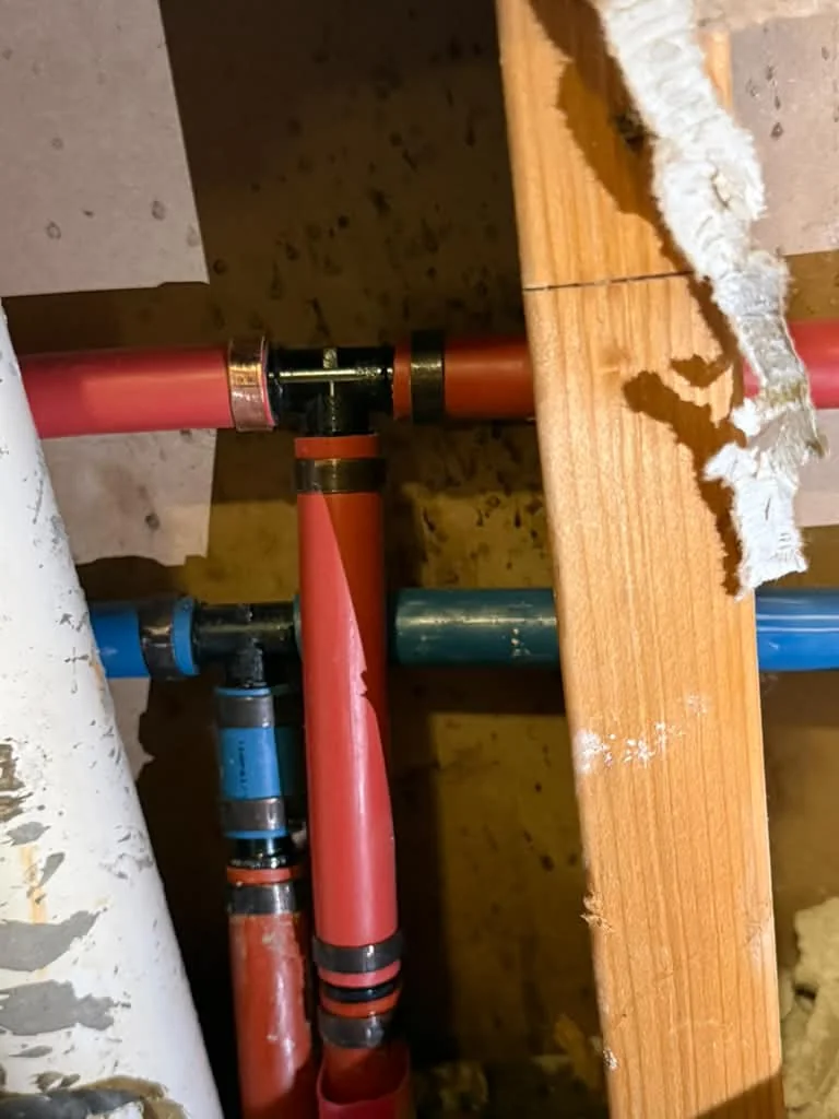 An opened interior wall showing new red and blue PEX and copper stubs run between studs