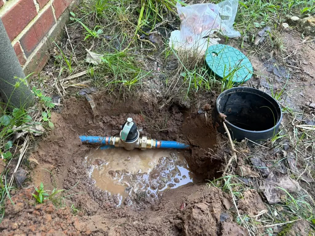 A blue poly water service line with a brass coupling lying in a shallow excavation