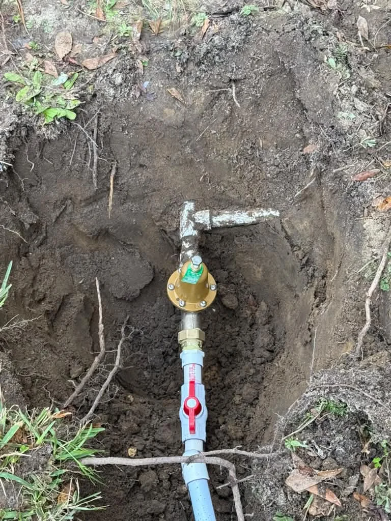 A water meter and shutoff valve exposed in a hand-dug hole with new service line connected