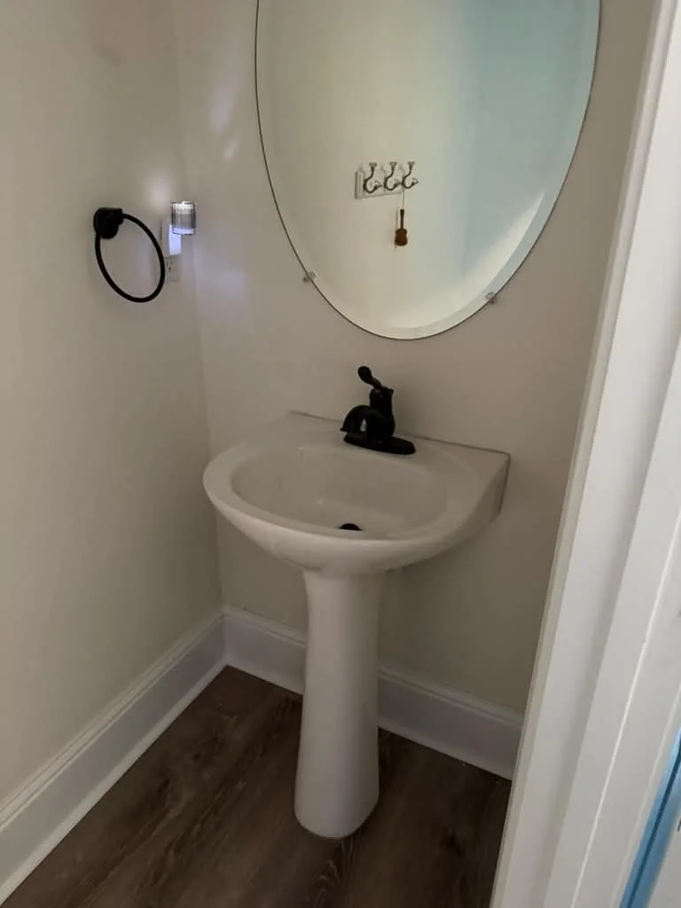 A finished pedestal sink with a dark bronze faucet against a pale wall on wood-look flooring