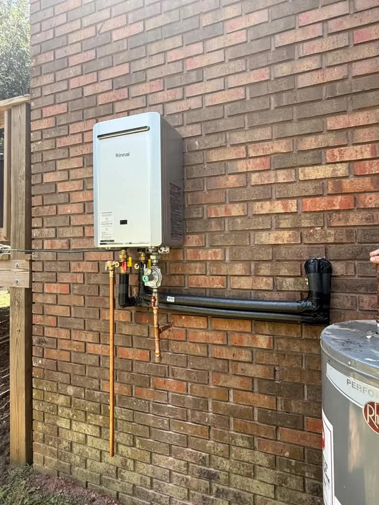 A Rinnai tankless water heater mounted on red brick with gas piping, isolation valves and a condensate line