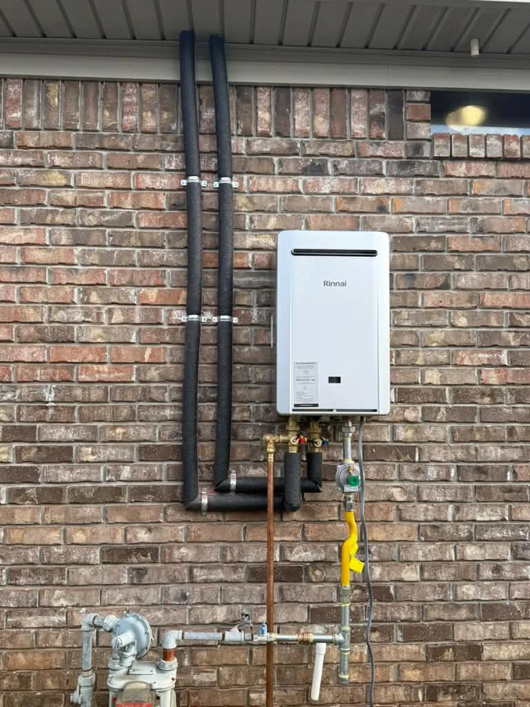 A tankless water heater on an interior brick wall with black gas pipe running up to the ceiling