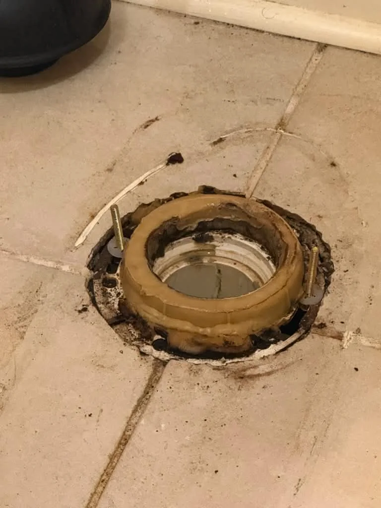 An open toilet flange in a tiled floor with the wax ring removed, ready for a reset