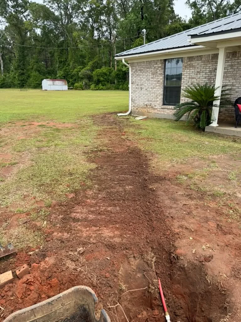 A freshly backfilled trench running across a lawn toward a white brick house
