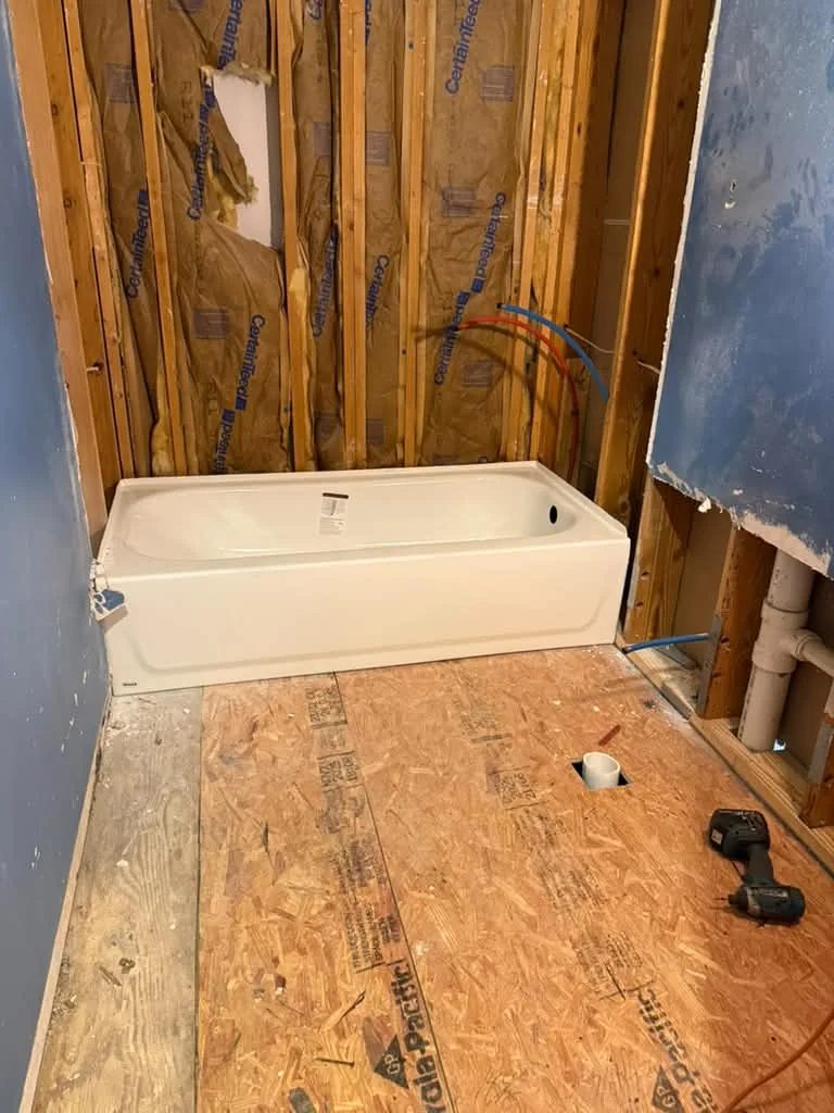 A new white bathtub set in a framed alcove on a subfloor, waste line roughed in