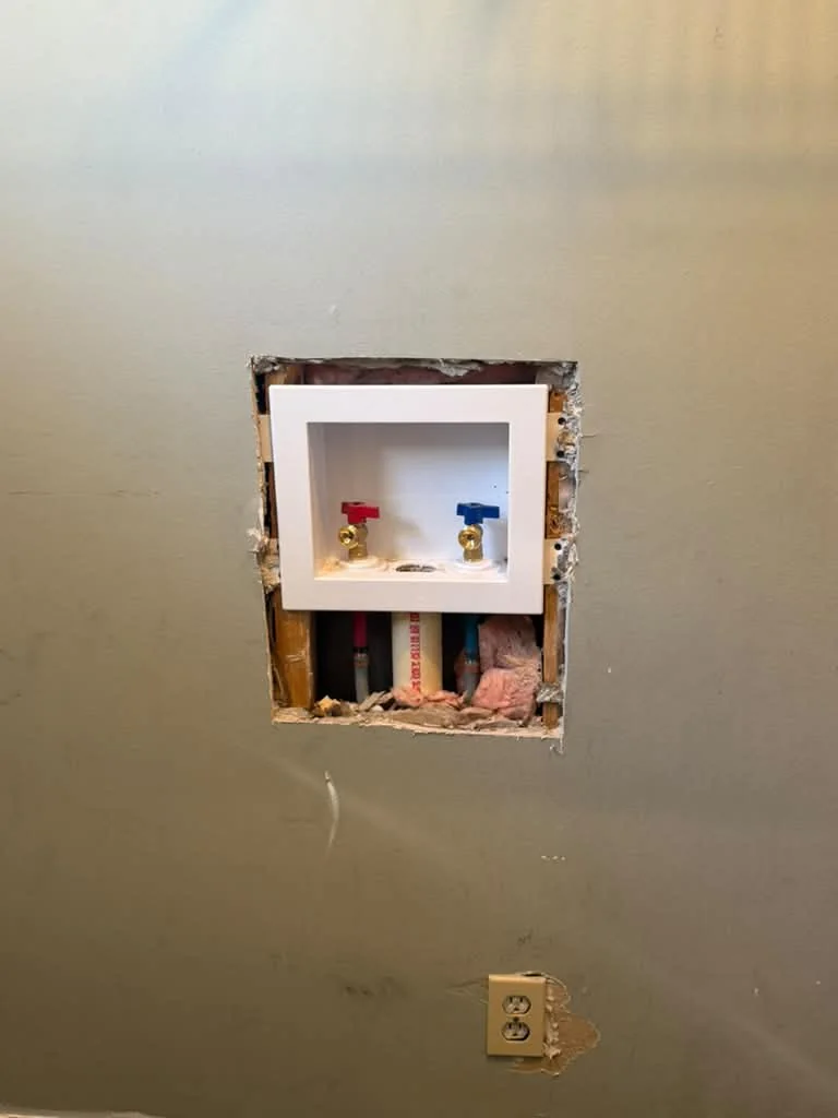 A new washing machine outlet box set into an opened wall with red and blue shutoffs